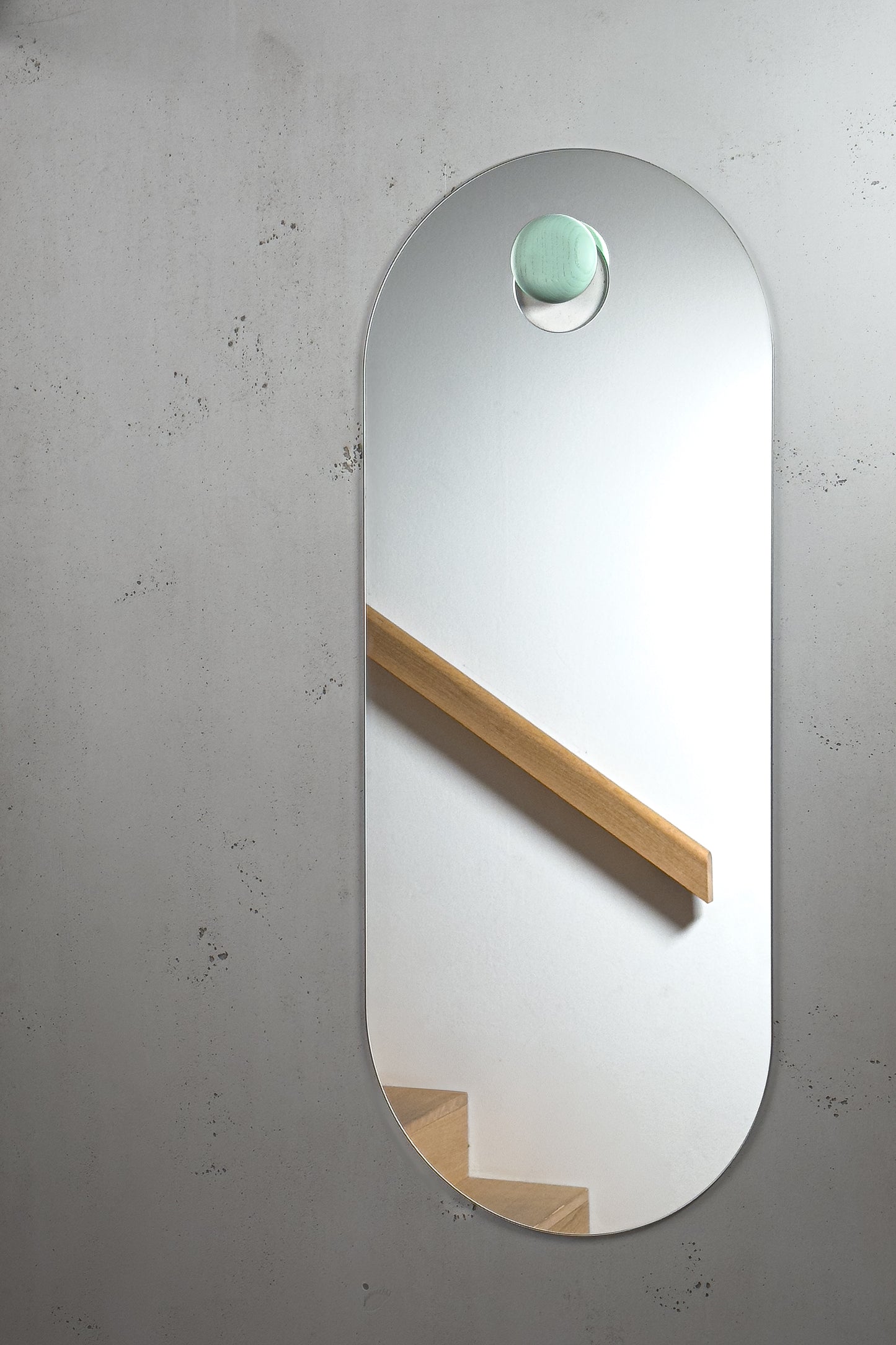 Unser wandhängende Spiegel im modernen Wohndesign hängt an einem salbeigrün gebeizten Holzknopf. Im Spiegelbild spiegelt sich ein Treppenhaus in Eiche