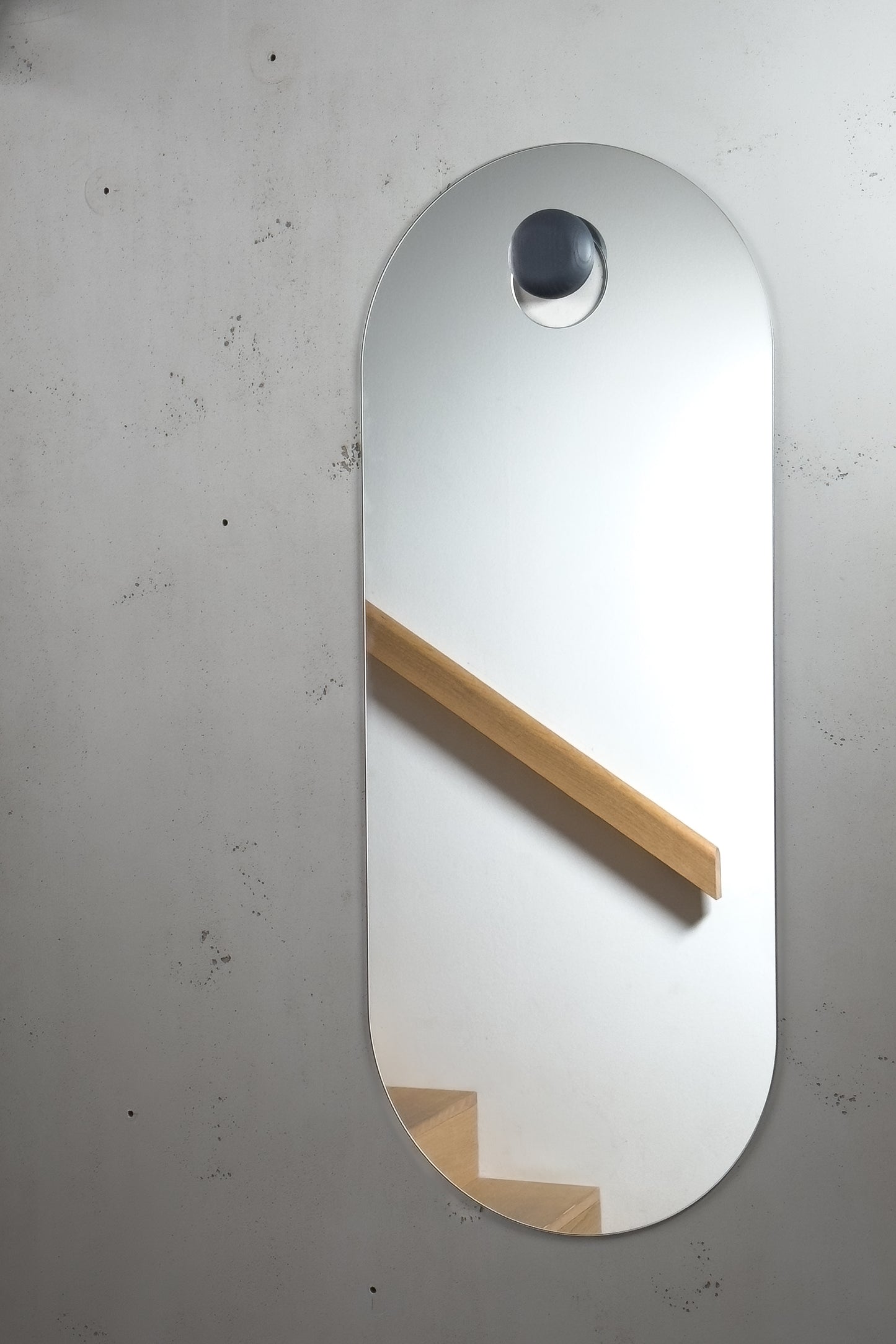 Unser stylischer Wandspiegel im Nordic Design hängt an einem schwarz gebeizten Holzknopf. Im Spiegelbild spiegelt sich eine moderne Treppe aus Eiche.