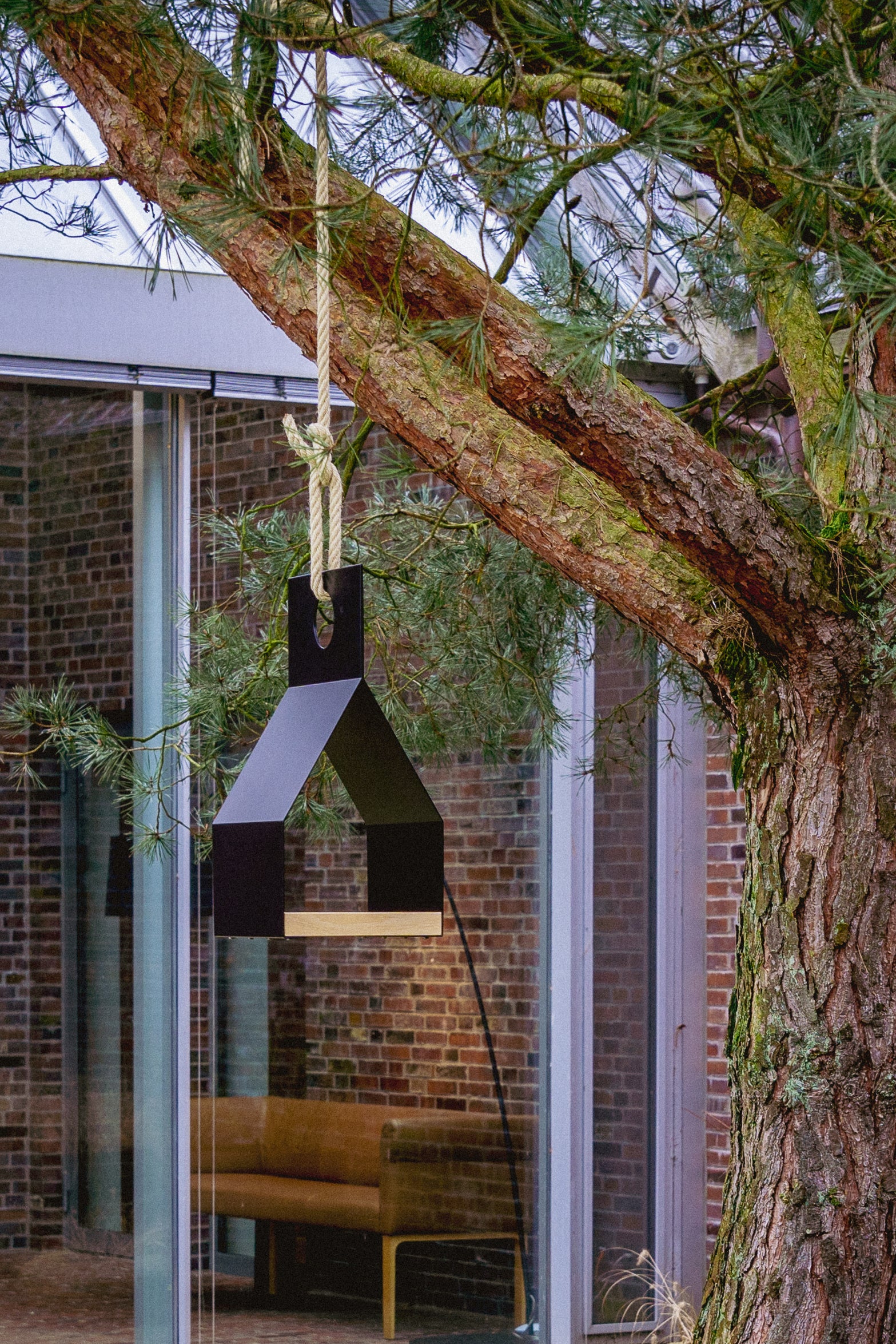 Unser modernes Vogelhaus FLY! an einer Kiefer hängend vor einem modernen Wintergarten, eingerichtet im Nordic Design