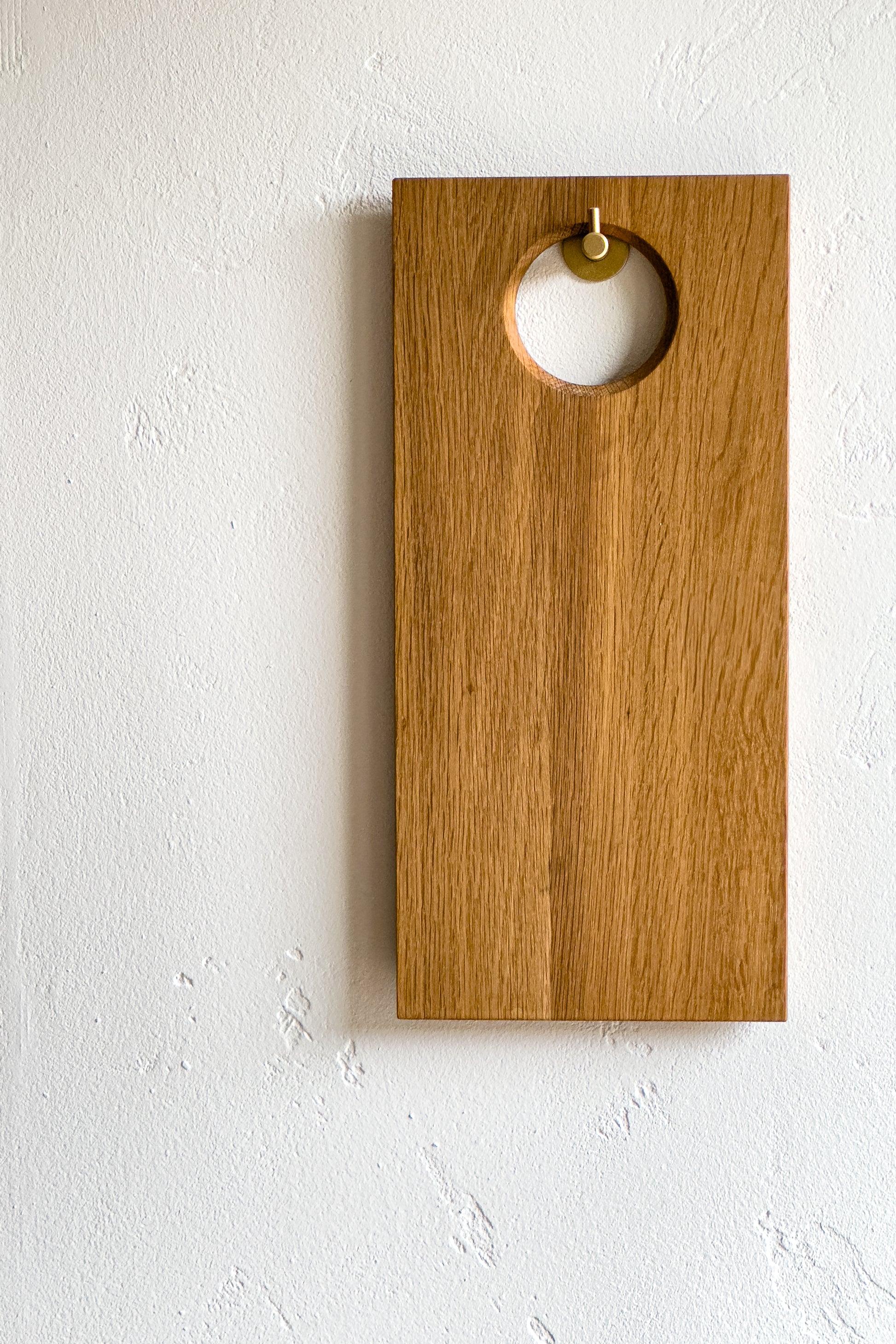 TRY! Minimalistisches Holzschneidebrett aus Eichenholz mit runder Aussparung, aufgehängt an einer weißen Wand. Schlichtes und modernes Design-Küchenaccessoire, ideal für Küche die moderne Küche, als Helfer oder Dekoration.