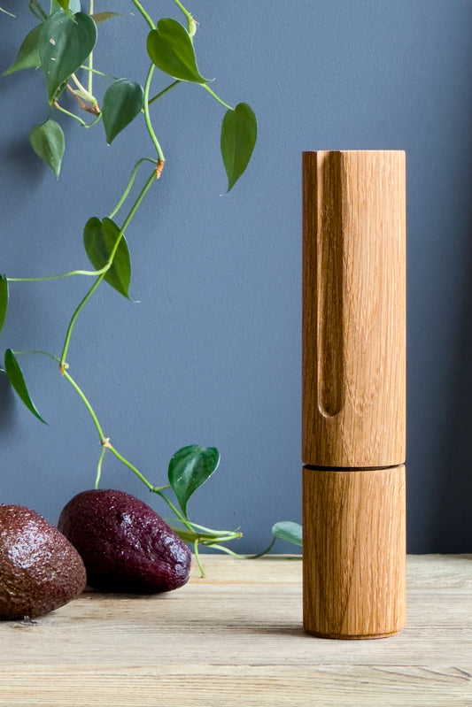 Tolles Geschenk für Hobbyköche: Handgefertigte Pfeffermühle aus Eichenholz in modernem Design, umgeben von grünen Pflanzen und Avocados. Die ideale Ergänzung für deine nachhaltige und natürliche Küche. Super Weihnachtsgeschenk!