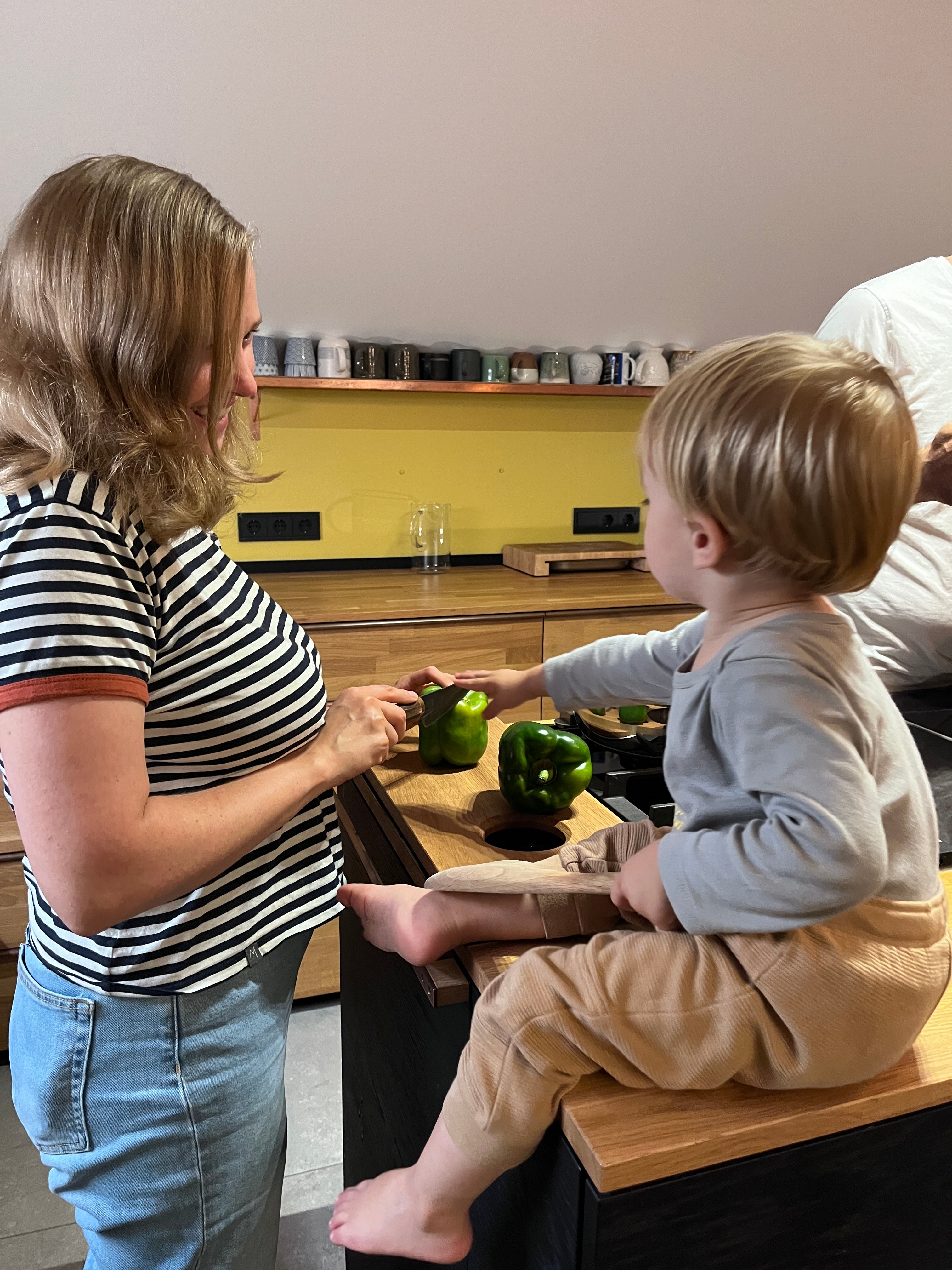 Das Foto zeigt eine Familie beim Kochen. Das Gemüse, zwei grüne Paprika werden auf unserem hochwertigen Schneidebrett TRY! aus Eiche geschnitten. Unser modernes Küchenaccessoire in Funktion.