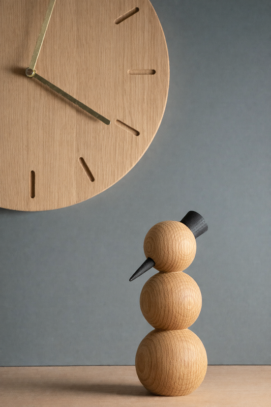 CLEAR Schneemann Skulptur aus Eiche als minimalistische Winterdekoration neben moderner Holzwanduhr.